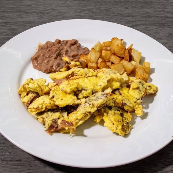 Scrambled eggs with refried beans and diced potatoes on a white plate.