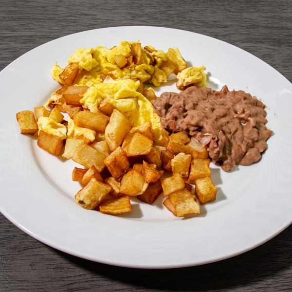 A white plate holds scrambled eggs, crispy home fries, and refried beans on a dark wooden table.