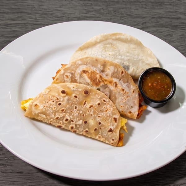 Three breakfast tacos with scrambled eggs and cheese, served with a side of salsa.